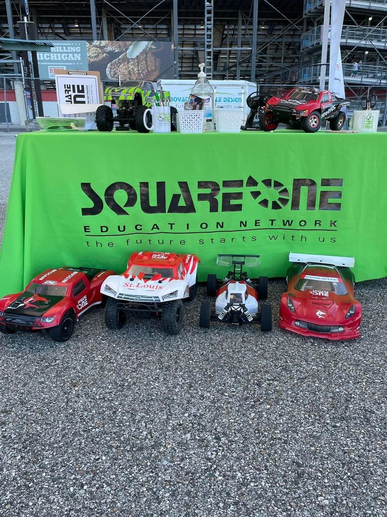 RC Cars sitting in front of a green table with the sign "Square one education network the future starts with us"